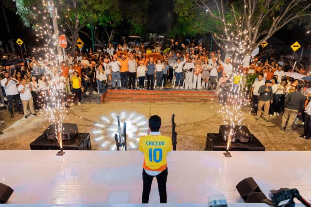 Carlos Caicedo en meeting político, de espaldas a la cámara, con camiseta que dice CAICEDO