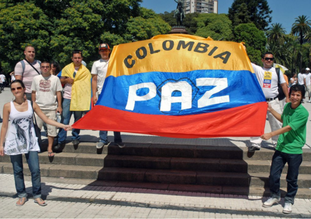 Bandera de Colombia, con la palabra PAZ, 6 personas sosteniendo la bandera
